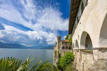 View of the courtyard and main entrance of the Hermitage of Santa Caterina del Sasso, a medieval monastery on a cliff overlooking Lake Maggiore, featuring stone archways and bell tower
