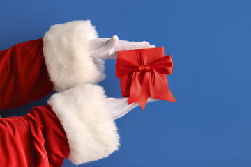 Santa hands with Christmas gift on color background, closeup