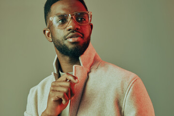 Stylish young African man in glasses wearing a modern grey jacket, showing confidence with a slight smile against a minimalistic background