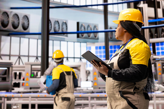 In automated factory, female engineer oversees operations with tablet, optimizing assembly line. Robotic arms and advanced machinery exemplify the future of Industry 4.0 and smart technology.