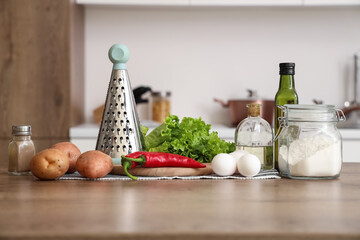 Grater with vegetables, eggs and oil on table in kitchen