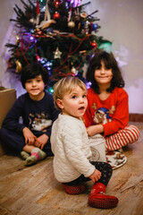 three small children sitting in front of Christmas tree at home