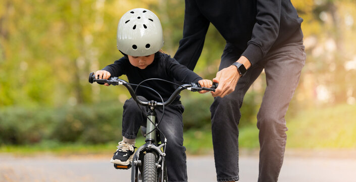 Father teaches young caucasian daughter to ride bicycle, sunlight