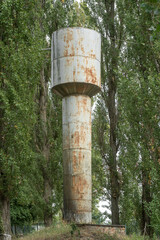 Fototapeta premium Rusted cylindrical water tower among tall poplar trees on a small hill.