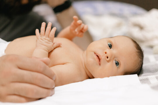Adorable caucasian newborn baby lying on bed with hands raised, Lifestyle moment of fatherhood.