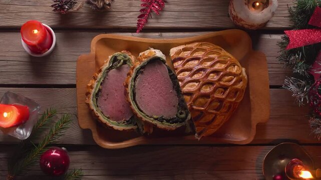 Top view of placing a plate with juicy Beef Wellington slices on a rough wooden table. Decorated with Christmas ornaments in a rustic style. Festive holiday dinner