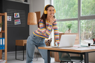 Thoughtful female graphic designer in headphones working with laptop at office