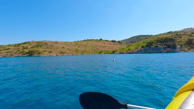 Kayaking in the mediterranean sea near the coast on a sunny day. Yellow kayak paddle dips rhythmically into the clear blue water, propelling the vessel forward along the picturesque coastliney
