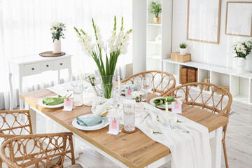 Stylish table setting with vase of Gladiolus flowers near window in kitchen
