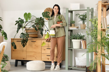 Beautiful young woman with watering can, gardening shovel and houseplant at home