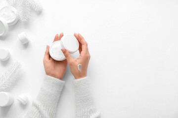 Female hands with jars of cosmetic cream and Christmas tree branches on grey background