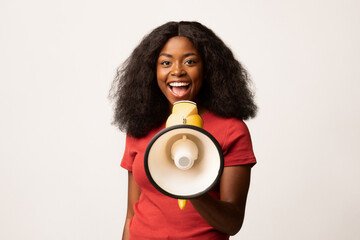 A cheerful young African American woman stands confidently, holding a loudspeaker while sharing...