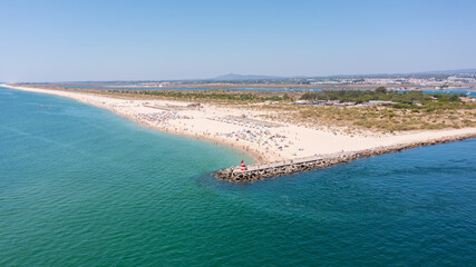 Scenic beach view with golden sands and turquoise waters, featuring a jetty and sunbathers enjoying a sunny day outdoors. Tavira Portugal Algarve