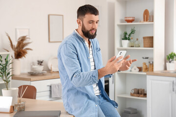 Young bearded man working with mobile phone in kitchen