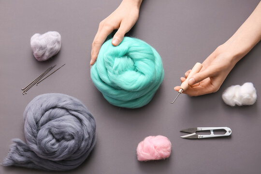 Female hands with different wool for felting, needles and thread cutter on grey background