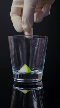 bartender gloved hand placing green fruit slice into glass on dark background, minimalistic preparation of drink or dessert for cocktail recipes, bar concept, culinary process, gastronomy visual