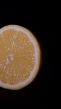 Rotating lemon half on black background in vertical video. Citrus slice spinning in motion with visible pulp, juice, texture on dark backdrop for food, beverage, ingredient, nutrition themes