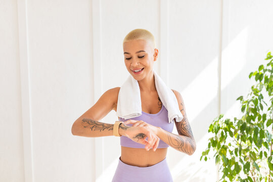 Portrait of sporty young lady checking her watch or fitness tracker after home workout, standing in living room interior, copy space. Athletic woman leading healthy lifestyle