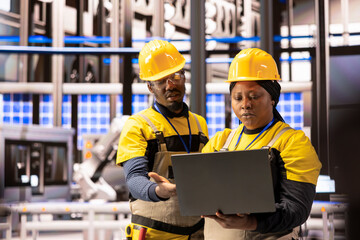 Engineers supervise manufacturing, using real time data to optimize robotic arm automation, assembly line efficiency and industrial plant operations. Industry 4.0 experts working together on laptop.