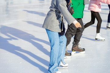 Naklejka premium Close-up of skating lesson with woman and instructor on ice rink during sunny winter day. Concept of beginner ice skating and personal coaching session, fun and outdoor winter lifestyle