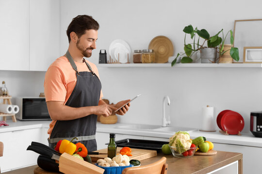 Handsome bearded man with tablet computer cooking in kitchen