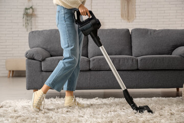 Young woman cleaning carpet with vacuum cleaner at home