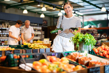 Young woman shopper choosing zucchini in grocery store
