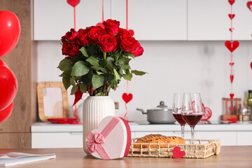 Vase with beautiful rose flowers, glasses of wine, croissants and gift box for Valentine's Day on table in kitchen
