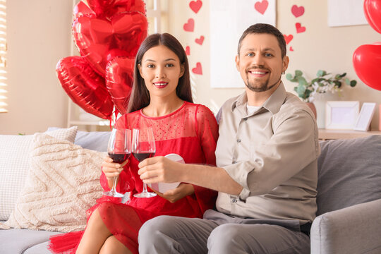 Young couple with wine sitting at home on Valentine's Day