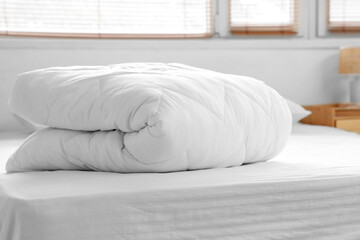 Folded white blanket on bed near window in bedroom