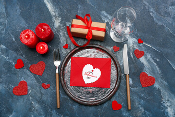 Table setting with candles, gift box and decorative hearts for Valentine's Day celebration on blue grunge background