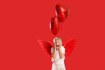 Obraz premium Cute little shocked boy dressed as cupid with heart-shaped balloons on red background. Valentine's Day celebration