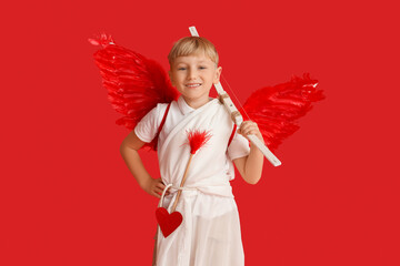 Obraz premium Cute little happy boy dressed as cupid with bow and arrow on red background. Valentine's Day celebration