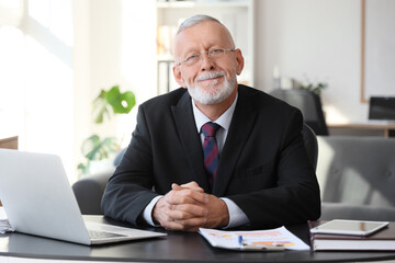 Obraz premium Senior businessman with clasped hands sitting at table in office