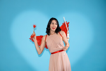Obraz premium Beautiful young happy woman dressed as cupid with bow and arrow on blue background. Valentine's Day celebration