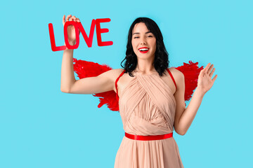 Obraz premium Beautiful young happy woman dressed as cupid with word LOVE on blue background. Valentine's Day celebration