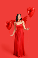 Obraz premium Beautiful young happy woman dressed as cupid with heart-shaped balloons on red background. Valentine's Day celebration