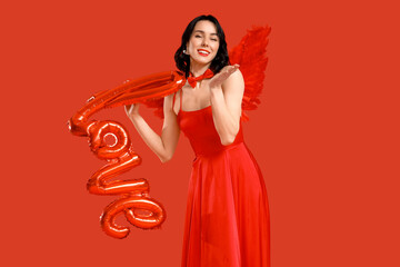 Obraz premium Beautiful young happy woman dressed as cupid with word LOVE made of balloons on red background. Valentine's Day celebration