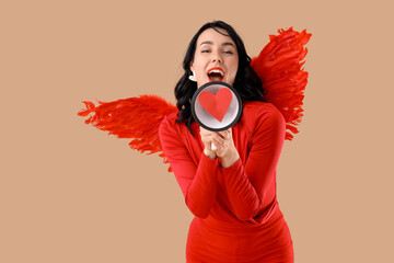 Obraz premium Beautiful young happy woman dressed as cupid with megaphone on beige background. Valentine's Day celebration