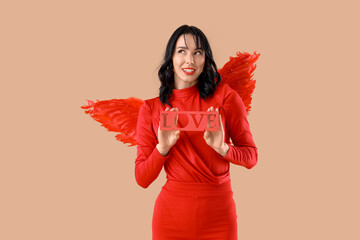 Obraz premium Beautiful young happy woman dressed as cupid with word LOVE on beige background. Valentine's Day celebration