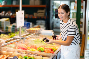 Young woman shopper choosing eggplants in grocery store
