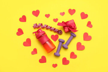 Composition with dumbbells, measuring tape, gift box and red hearts on yellow background. Valentine's Day celebration