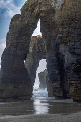 detail of a rock arches and towering cliffs at As Catedrais Beach in Ribadeo, Spain, captured at low tide with soft light, ocean waves, and dramatic natural formations