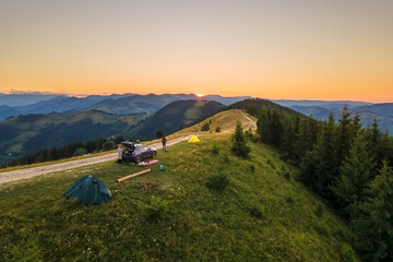 Fototapeta premium Sunset mountain landscape with tourist camping tents and a SUV car on hillside campsite at bright sunny evening. Offroad adventure