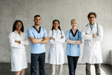Multiracial medical team male and female doctors in workwear posing at clinic while having team-building, cheerfully smiling at camera. Professions, occupations, healthcare concept