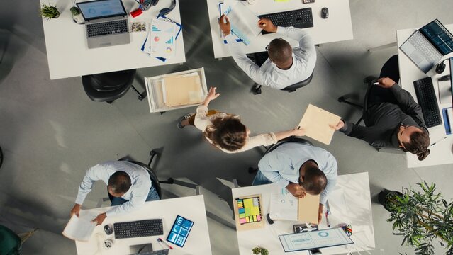 Top down view of colleagues checking archived files in workplace, reviewing charts and analytics. Employees discuss project progress, report writing and data visualization.