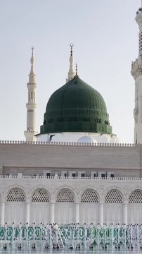 The majestic Prophet's Mosque (Al-Masjid an-Nabawi) in Medina, showcasing the Green Dome, modern retractable umbrellas, and thousands of devout pilgrims in prayer and transit.