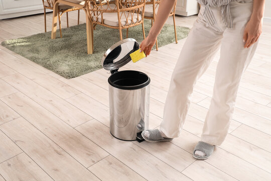 Woman throwing cleaning sponge into trash bin in kitchen