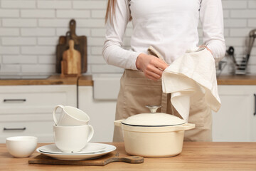 Woman wiping clean dishes with napkin in kitchen