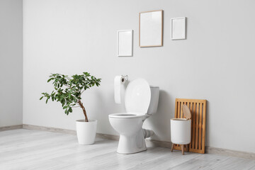 Interior of light restroom with toilet bowl, blank frames and bin